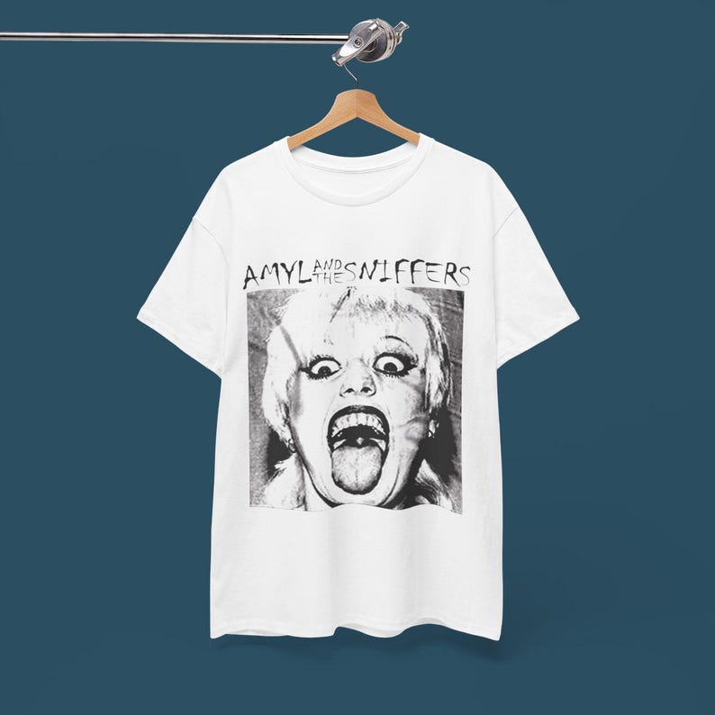 May include: White t-shirt with a black and white image of a woman with her tongue sticking out. The text "Amyl and the Sniffers" is printed above the image.