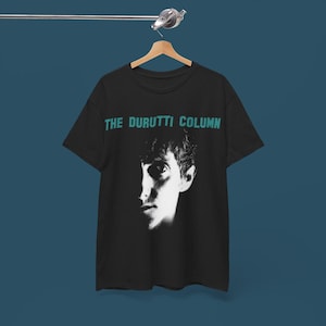 Może przedstawiać: Czarny T-shirt z białym obrazem twarzy mężczyzny i tekstem "THE DURUTTI COLUMN" w kolorze turkusowym.