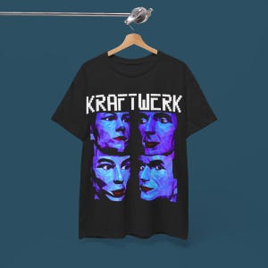 Könnte beinhalten: Schwarzes T-Shirt mit einem weißen, pixelartigen "KRAFTWERK"-Text und vier blauen und violetten, pixelartigen Gesichtern.