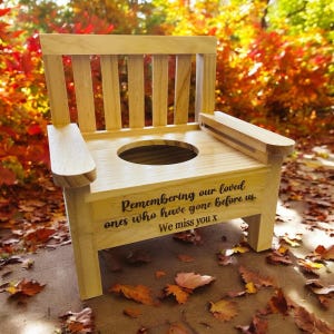 May include: Wooden memorial chair with a seat shaped like a toilet bowl. The chair is engraved with the words "Remembering our loved ones who have gone before us. We miss you x".