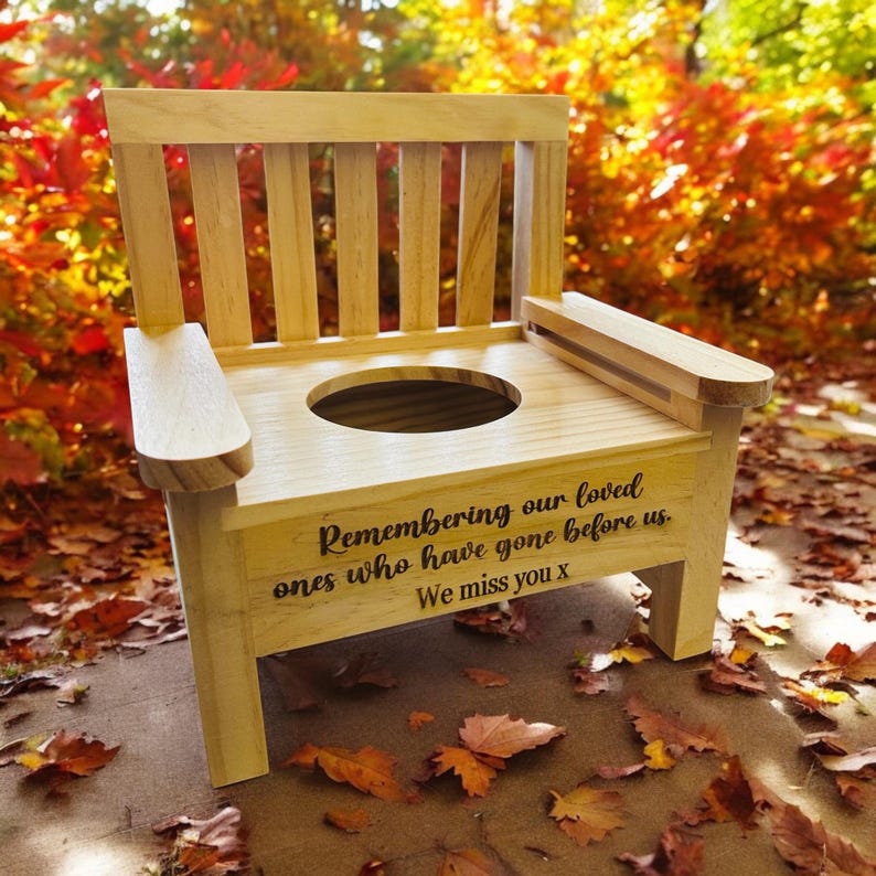 May include: Wooden memorial chair with a seat shaped like a toilet bowl. The chair is engraved with the words "Remembering our loved ones who have gone before us. We miss you x".