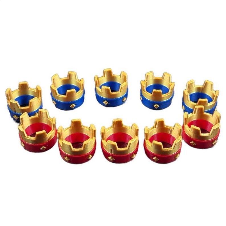 May include: Ten small, decorative crown-shaped objects. The crowns are gold-colored with a blue or red base. Each crown has a diamond-shaped accent on the base. The crowns are arranged in two rows on a white background.