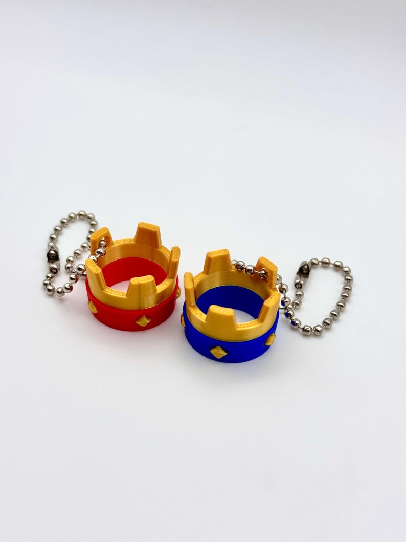 May include: Two miniature crown keyrings. One is red with gold accents, the other is blue with gold accents. Both have a diamond pattern and are attached to a silver ball chain.