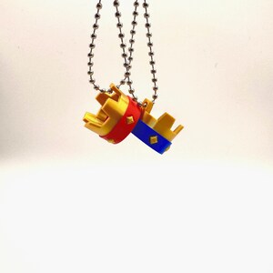 May include: Two miniature crown keyrings. One crown has a red band, the other has a blue band. Both crowns are gold with silver chain attachments. The keyrings are suspended against a white background.