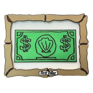 May include: A framed illustration of a green dollar bill with a seashell in the center. The frame is made of brown wood and has the text "First Dollar" at the bottom.
