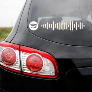 Puede incluir: Un coche negro con un logotipo de Spotify blanco y un código de barras blanco en la ventana trasera.