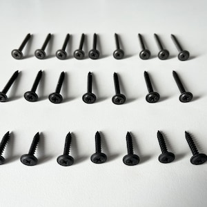 Może przedstawiać: Zestaw 24 czarnych śrub z płaską główką i gniazdem krzyżakowym. Śruby mają srebrne wykończenie i głowicę z podkładką.