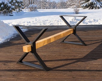 May include: A table base featuring two black metal X-shaped legs connected by a single horizontal wooden beam. The structure is designed to support a tabletop, showcasing a combination of dark matte metal and a natural light brown wood finish.
