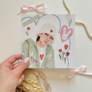 May include: A digital illustration of a person wearing a green jacket and a white bucket hat. The person has a heart-shaped patch on their shirt and is surrounded by flowers and hearts. The text "TEUNGHUN" is written on a sticker in the top left corner of the image.