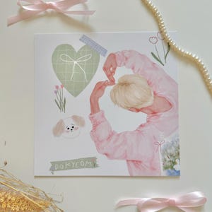 May include: An illustrated print in pink and green featuring a person making a heart shape with their hands, a green heart with a white bow, a white dog with brown ears, and the text "DOKYEOM".