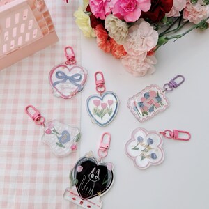 Pu&ograve; includere: Un set di sei portachiavi in acrilico trasparente con diversi design. I portachiavi presentano un cuore con fiori, un fiore con il testo "Hope", un fiore con il testo "Sweet as Pie", un cuore con un gatto nero, un cuore con il testo "Always in My Heart", e un fiore con il testo "Best Friends".