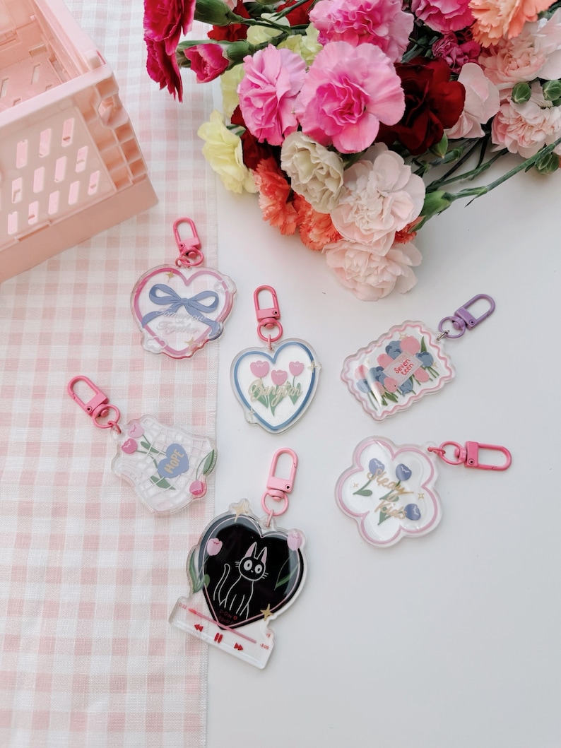 Pu&ograve; includere: Un set di sei portachiavi in acrilico trasparente con diversi design. I portachiavi presentano un cuore con fiori, un fiore con il testo "Hope", un fiore con il testo "Sweet as Pie", un cuore con un gatto nero, un cuore con il testo "Always in My Heart", e un fiore con il testo "Best Friends".