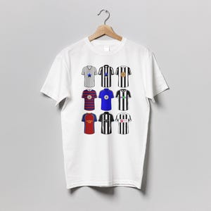 May include: White t-shirt featuring nine colorful soccer jerseys. The jerseys are in various colors, including blue, red, black, and white, with different designs. The t-shirt is hanging on a wooden hanger against a gray background.