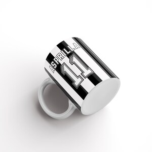 May include: A white ceramic mug with a black and white striped design. The mug has the name "Asprilla" and the number "11" printed on it.