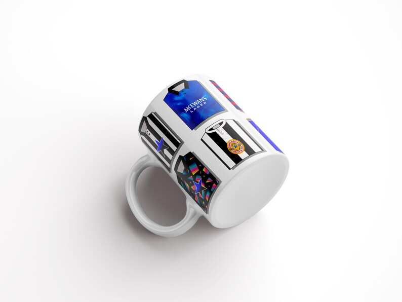 Peut inclure: Une tasse en c&eacute;ramique blanche avec un motif de diff&eacute;rents maillots de football, dont un maillot bleu avec le texte "McEwans Lager" dessus.