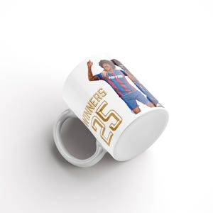 May include: White ceramic mug with a person in a blue and red sports uniform. The mug has the text "WINNERS 25" in gold. The person is celebrating. A sports-themed gift. The mug is a standard size.