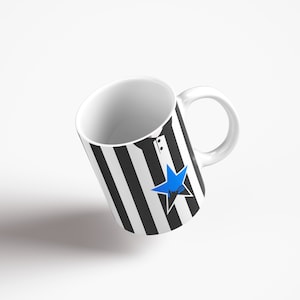 May include: A white ceramic mug with a black and white striped design and a blue star. The mug has a handle.