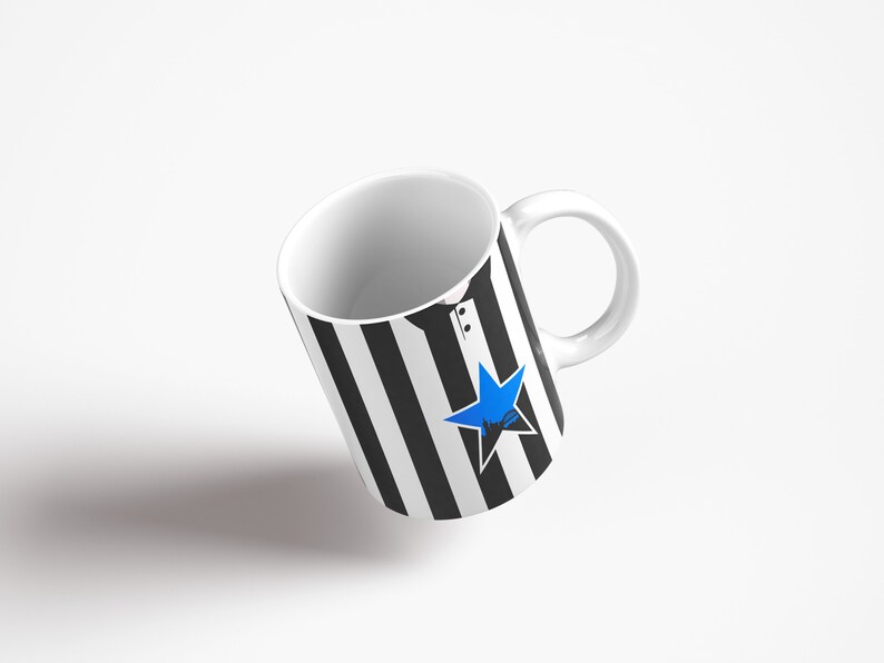 May include: A white ceramic mug with a black and white striped design and a blue star. The mug has a handle.
