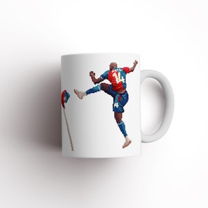 May include: White ceramic mug featuring a graphic of a football player kicking a ball. The player is wearing a red and blue jersey with the number 14 on it.