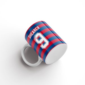 May include: White ceramic mug with a red and blue striped design. The mug features the name "SHEARER" and the number "9" in white.