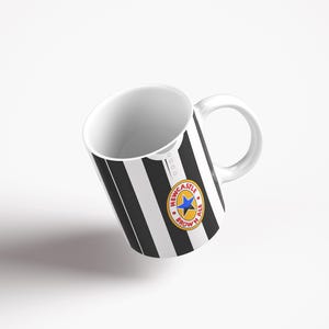 May include: A white ceramic mug with a black and white striped design. The mug has a Newcastle Brown Ale logo on the front.