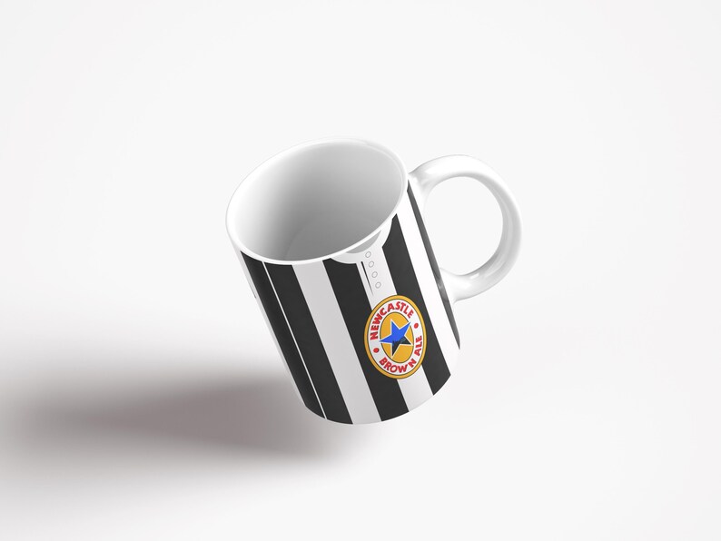May include: A white ceramic mug with a black and white striped design. The mug has a Newcastle Brown Ale logo on the front.