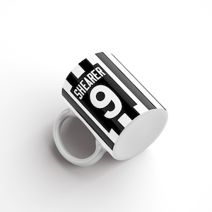 May include: White ceramic mug with a black and white striped design. The mug has the text "SHEARER 9" printed on it.