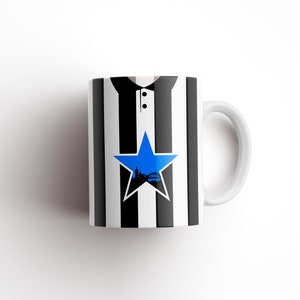 May include: White ceramic mug with a black and white striped design. A blue star with a city skyline inside is centered on the mug.