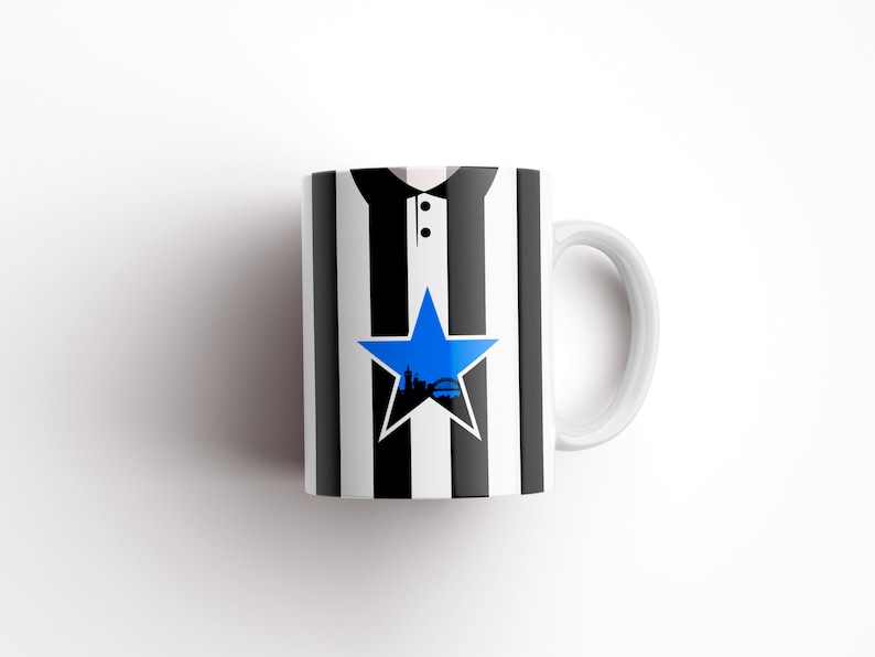 May include: White ceramic mug with a black and white striped design. A blue star with a city skyline inside is centered on the mug.
