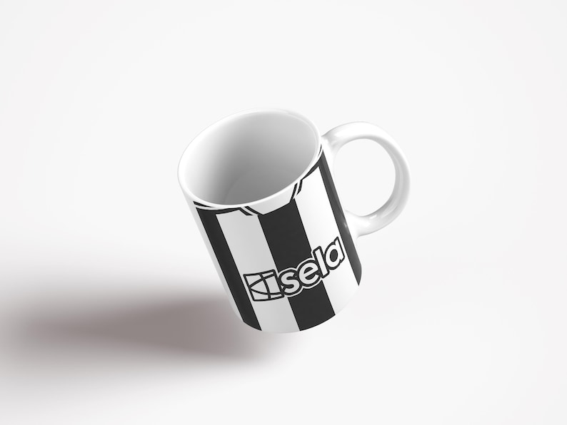 May include: White ceramic mug with a black and white striped design. The design features a black and white soccer jersey with the word "sela" printed on it.