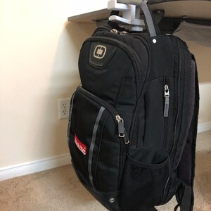 May include: A black backpack with a red "Makita" logo hanging from a white plastic hook attached to a desk.