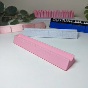 May include: A pink plastic organizer with four compartments. The organizer is designed to hold small items, such as pens, pencils, or other office supplies.