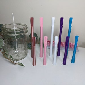 May include: A set of ten candle wicks with different coloured tips. The wicks are arranged in a row on a white surface. The wicks are all the same size and shape, but they have different coloured tips. The colours of the tips are: rose gold, pink, white, purple, and blue.
