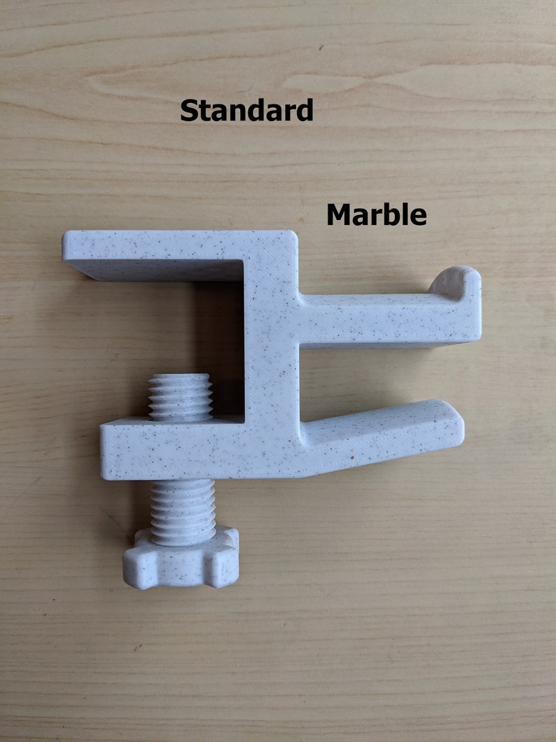 May include: A white plastic clamp with a speckled finish, labeled "Standard" and "Marble". The clamp has a screw with a hexagonal head.