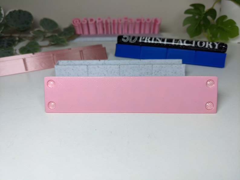 May include: A pink rectangular sign with two small white circles on each end. The sign is sitting on a white surface.