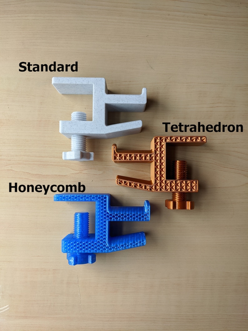 May include: Three 3D printed desk clamps in different colors and patterns. The white clamp is labeled "Standard", the orange clamp is labeled "Tetrahedron", and the blue clamp is labeled "Honeycomb".
