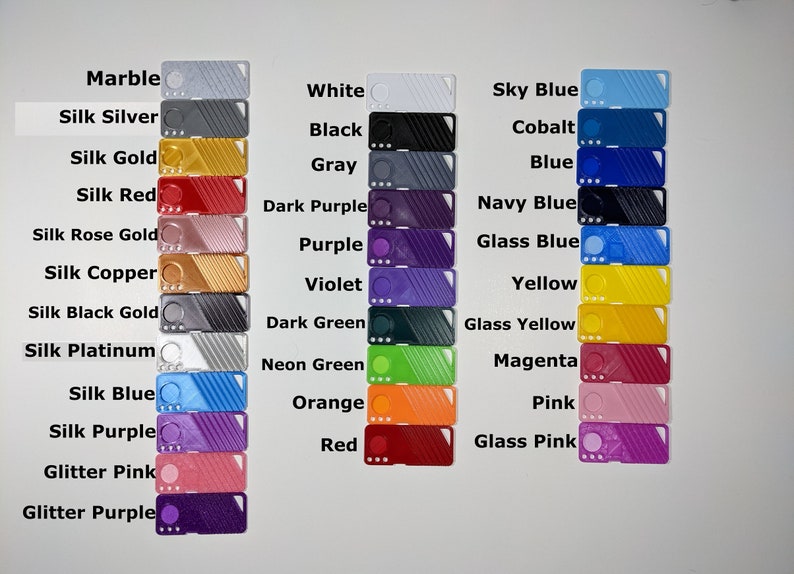 May include: A color chart of 24 different colors of plastic filament for 3D printing. The colors include marble, silk silver, silk gold, silk red, silk rose gold, silk copper, silk black gold, silk platinum, silk blue, silk purple, glitter pink, glitter purple, white, black, gray, dark purple, purple, violet, dark green, neon green, orange, red, sky blue, cobalt, blue, navy blue, glass blue, yellow, glass yellow, magenta, pink, and glass pink.