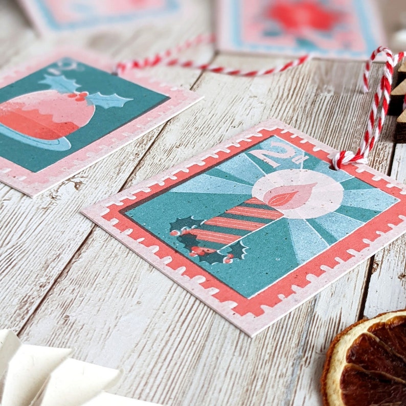 Pu&ograve; includere: Due etichette regalo di Natale con un bordo rosa e rosso. Un'etichetta presenta una candela a strisce rosso e bianco con una fiamma e agrifoglio. L'altra etichetta presenta un budino di Natale rosso e bianco con agrifoglio.