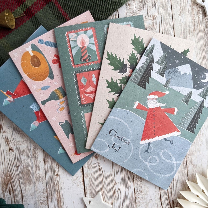May include: Set of four Christmas cards featuring illustrations of a candle, holly, a snowman, and Santa Claus. The cards are printed on a textured paper stock and have a vintage aesthetic. The text on the cards reads "Christmas Joy!"