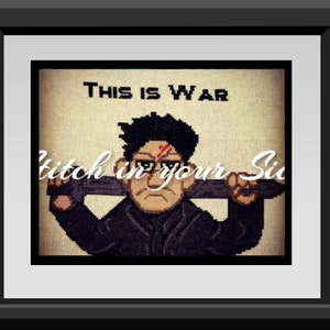 May include: Cross-stitch artwork framed in black. The image features a pixelated illustration of a stern-faced figure with the text "THIS IS WAR" above and "Stitch in your Si" below. The figure has a scar and is holding a cross-stitch.
