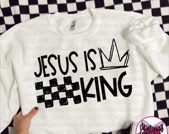 May include: White crew neck sweatshirt featuring the text "JESUS IS KING" in black, with a crown graphic. The word "KING" is styled with a hashtag and a checkered pattern. The background is a black and white checkered pattern.