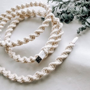 Puede incluir: Un cable de carga trenzado blanco con un conector USB. El cable está enrollado y colocado sobre una superficie blanca.