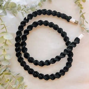 May include: A black braided charging cable with white USB connectors on each end. The cable is coiled and laid out on a white surface.