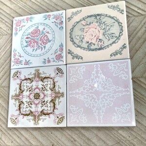 Op de afbeelding: Vier vierkante keramische tegels met bloemmotieven. De tegels hebben roze rozen, sierlijke randen en een kantachtig patroon op een roze achtergrond. Het kleurenpalet omvat roze, wit en vleugjes goud.