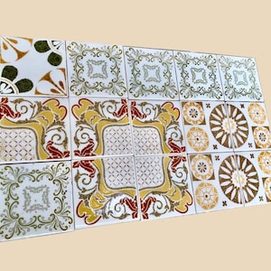 May include: A selection of square ceramic tiles with diverse decorative patterns. The tiles display ornate designs in gold, red, green, and brown on a white background. Some tiles feature floral and geometric motifs.
