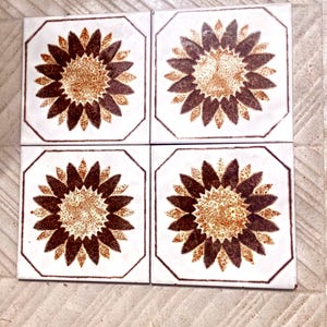 May include: Four square ceramic tiles with a white background and a brown and tan sunflower design. Each tile has a brown octagonal border. The sunflower has brown petals and a tan center. The tiles are arranged in a 2x2 grid.