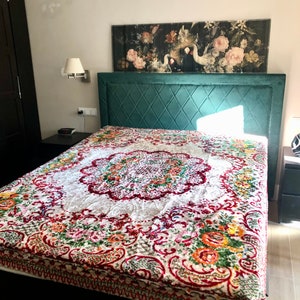May include: A bed with a teal headboard and a floral patterned bedspread. The bedspread features a white center with a red and floral border. A painting with flowers and swans hangs above the bed.