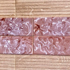 Può includere: Quattro piastrelle rettangolari caratterizzate da un motivo marmorizzato nei toni del rosa antico, marrone scuro e bianco. La superficie di ogni piastrella presenta una finitura liscia e lucida con striature di colore fluide e vorticose.