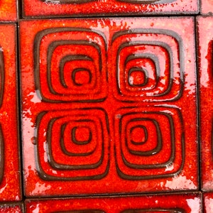May include: A collection of square ceramic tiles featuring a glossy, vibrant orange glaze. Each tile displays a repeating pattern of dark brown, recessed concentric squares that create a textured, geometric design across the surface.