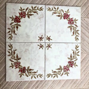 Op de afbeelding: Vier vierkante keramische tegels met een witte marmerlook achtergrond. Elke tegel heeft een hoekontwerp van rode rozen en goudkleurige bladeren. Kleine bloemaccenten bevinden zich in het midden van de tegels. Decoratieve tegels voor woondecoratie.